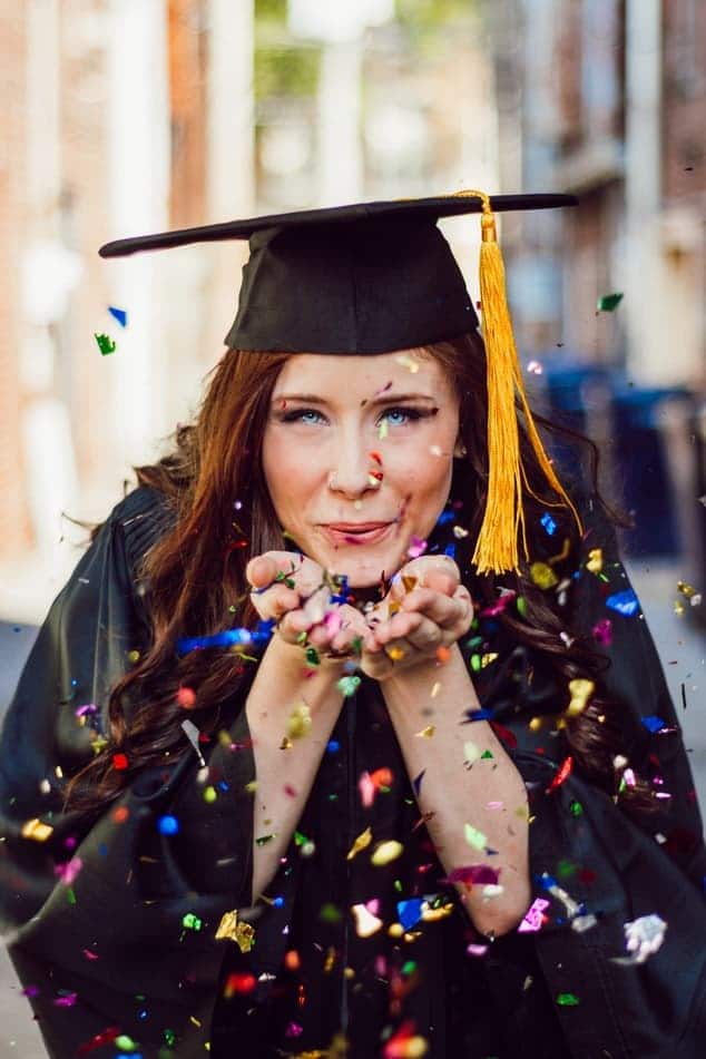 Woman in graduation gown blowing confetti
